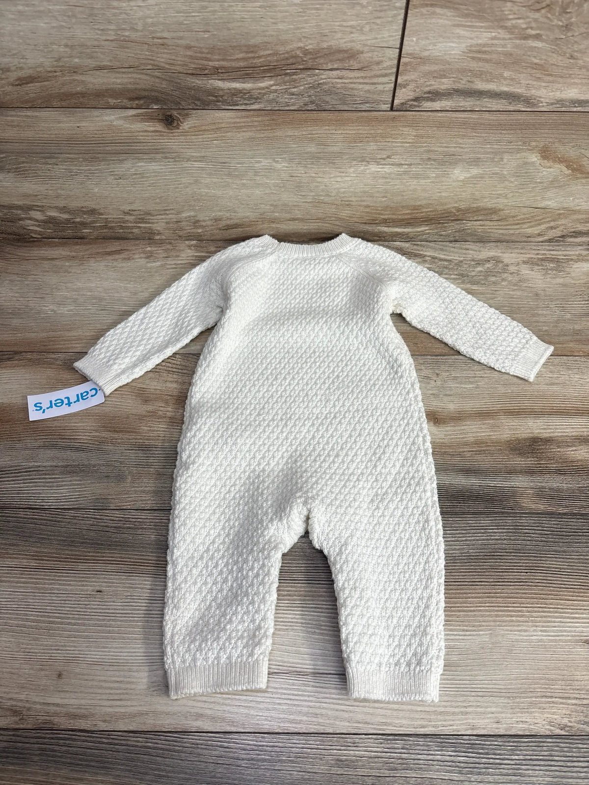 White Carter's baby onesie with textured knit, laid on wood floor
