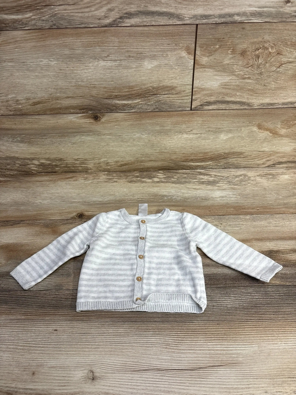 Light gray and white striped baby cardigan with wooden buttons on wood floor