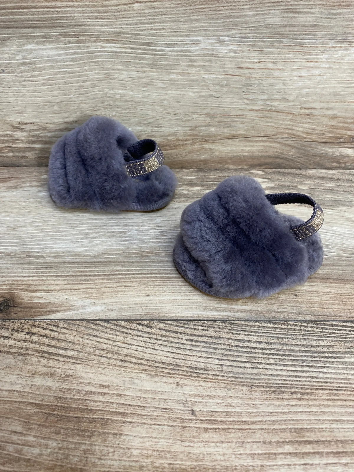 Front three-quarter view of grey UGG Fluff Yeah toddler slides showcasing soft sheepskin uppers and elastic heel straps on a wood background