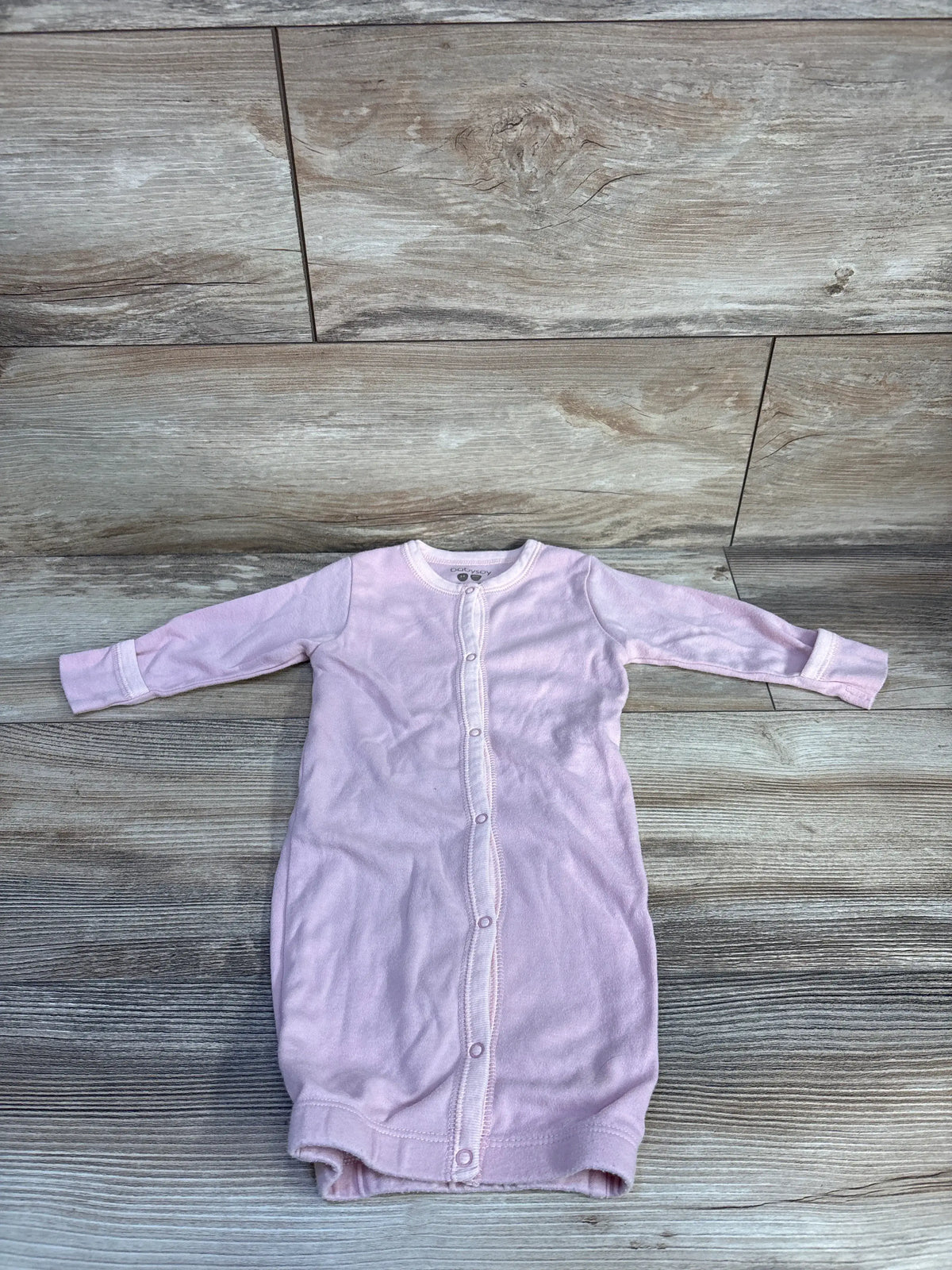 Front view of Babysoy solid pink snap sleep gown showcasing long sleeves and front snap closure on a wood-look floor