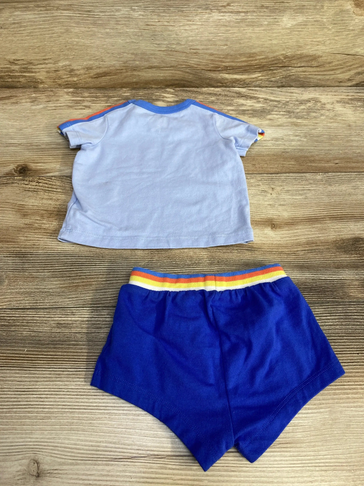 Back view of Cat and Jack newborn shirt and shorts showing rainbow elastic waistband and blue sleeve trim on wood background