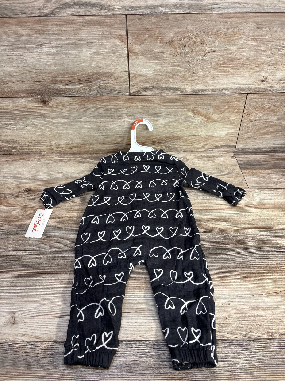 Black baby romper with white heart pattern on wooden floor, Cat & Jack brand tag visible