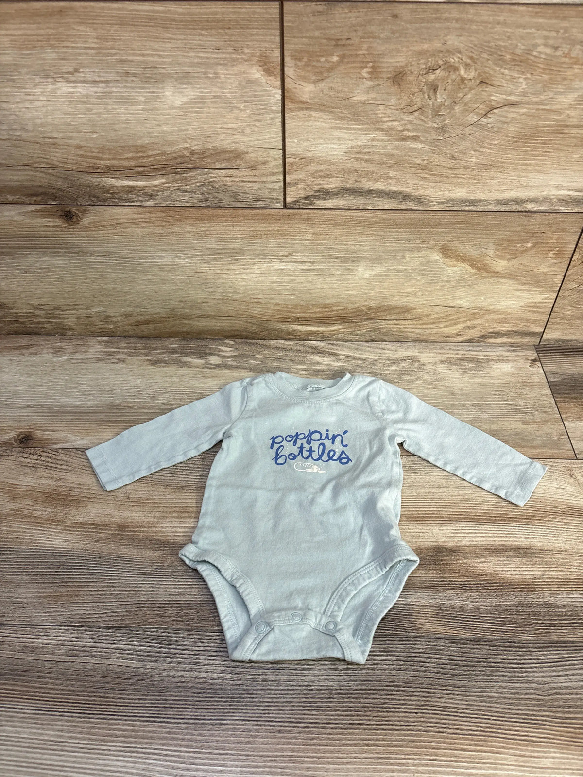 Front view of Carter’s green Poppin’ Bottles bodysuit with long sleeves, snap closures, and chest graphic on wood grain
