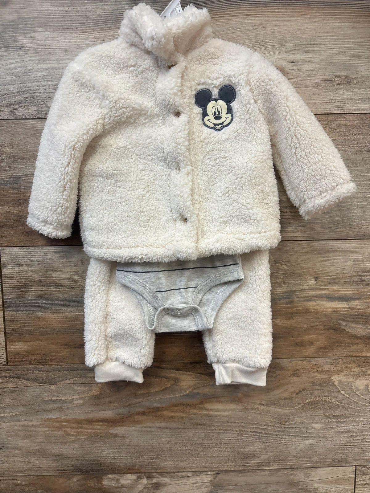 Front view of Disney Baby cream Mickey Mouse sherpa sweatshirt, bodysuit, and joggers laid flat on wood