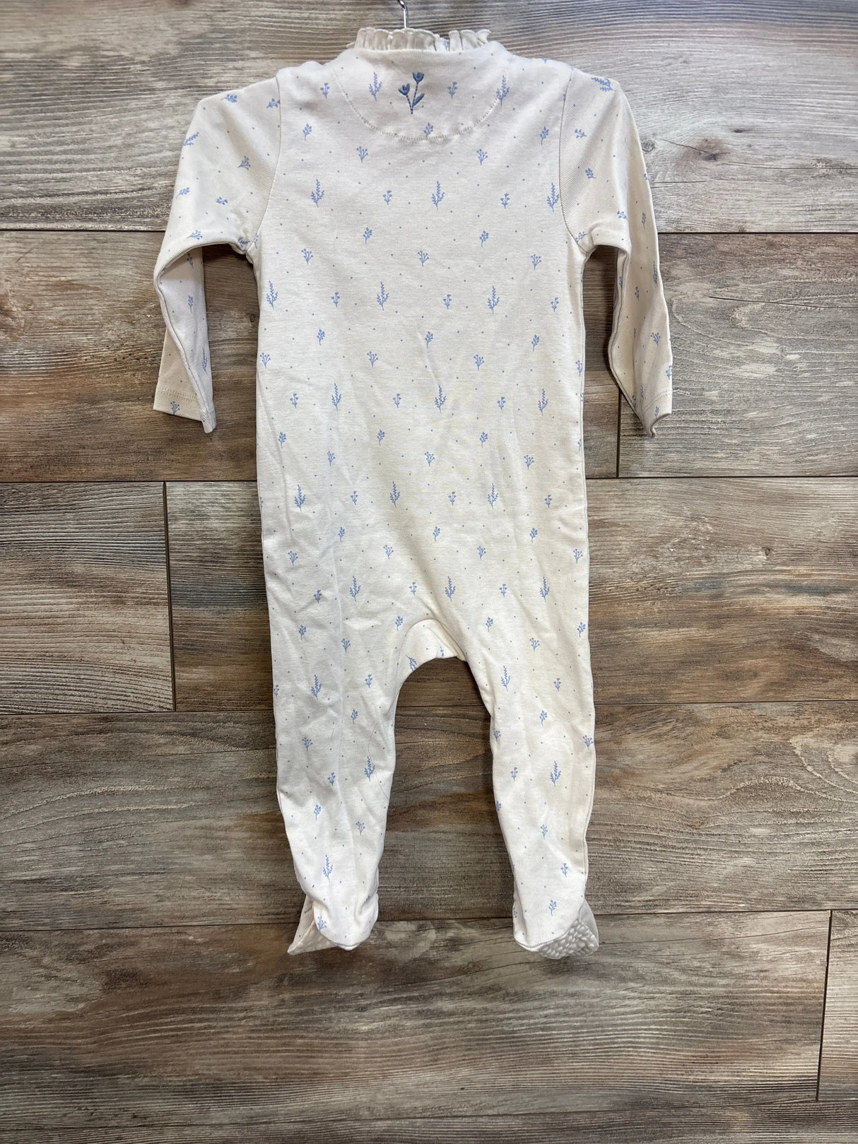 Front view of beige cotton footed baby sleeper with small blue sprig print and ruffle collar on wooden floor
