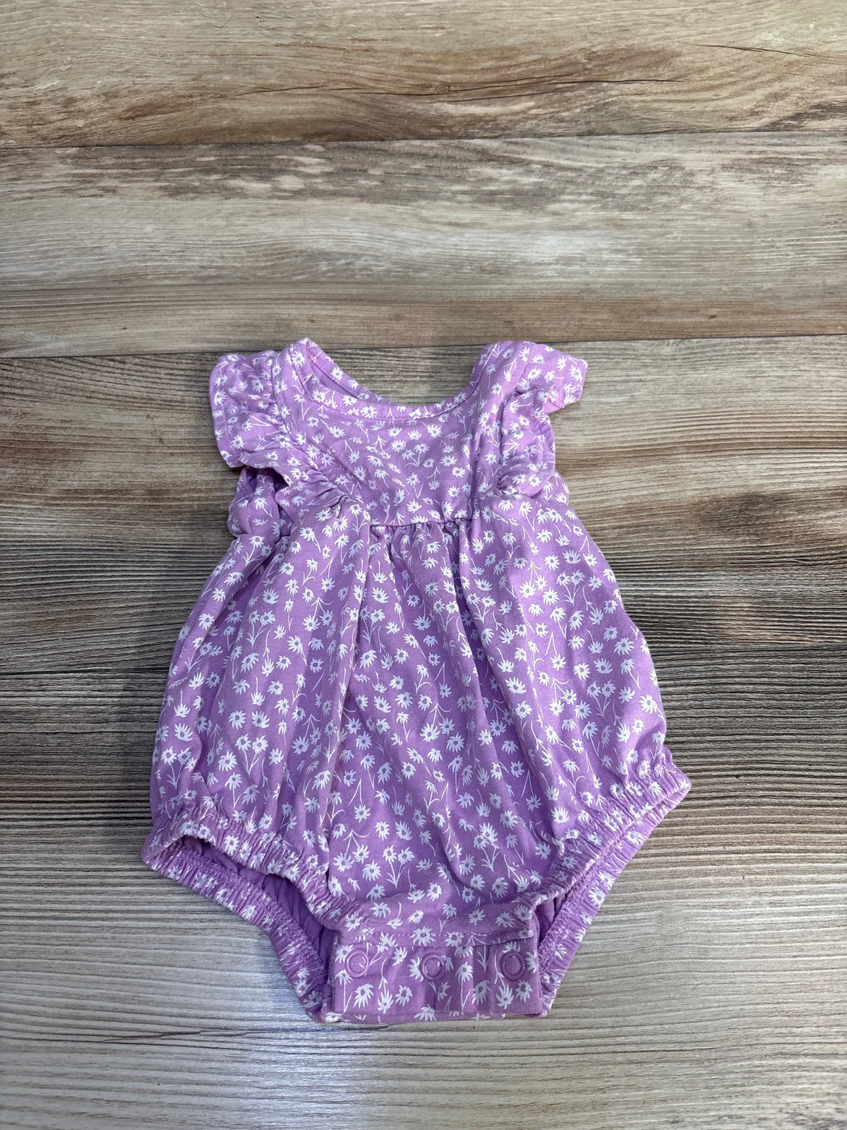 Front view of purple Okie Dokie bubble romper size 6 months with white floral print and gathered legs on wood background