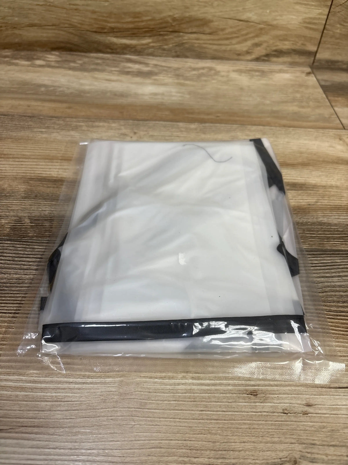 Front view of a white universal rain shade cover with black trim, packaged on a wooden surface