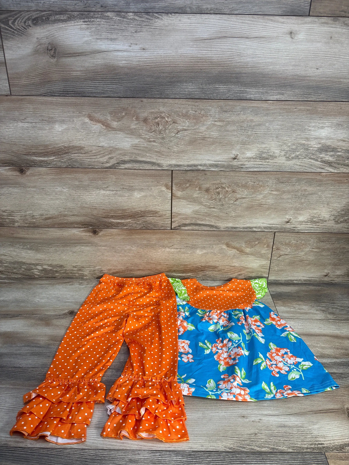 Top-down view of Waverly Scarlet two-piece dress and ruffle pants set showcasing orange polka dots and floral skirt on wood flooring