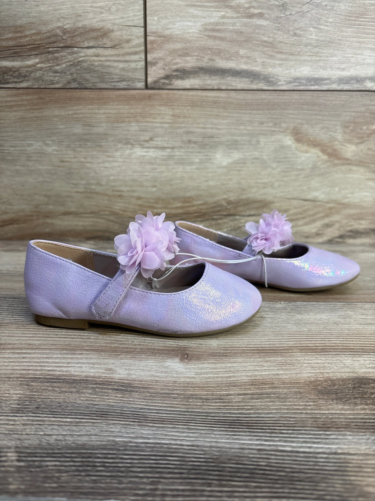 Side view of Gymboree lavender floral ballet flats showing iridescent glitter finish and pink fabric flower strap on wood background