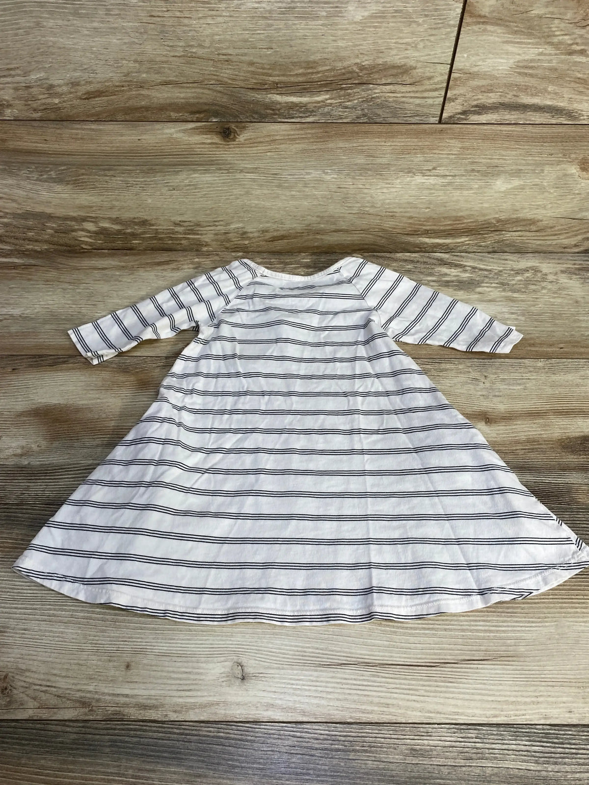 Flat lay of white toddler dress with thin navy stripes and long sleeves, size 3T, on light wood background