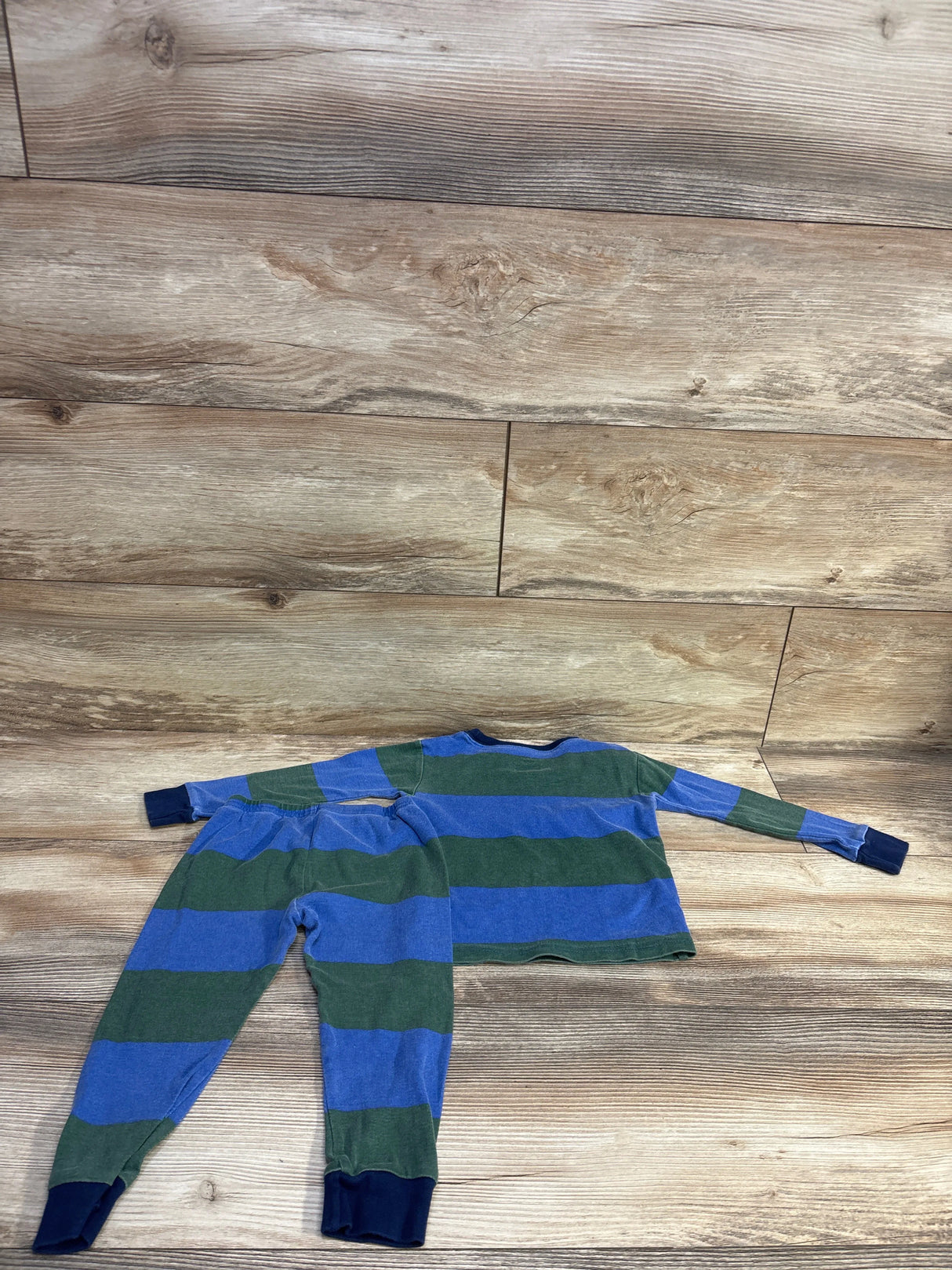 Flat lay of Carter’s 2-piece toddler pajama set with blue and green wide stripes and navy cuffs on wood floor