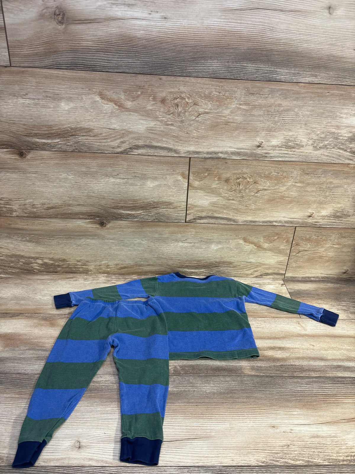 Flat lay of Carter’s 2-piece toddler pajama set with blue and green wide stripes and navy cuffs on wood floor
