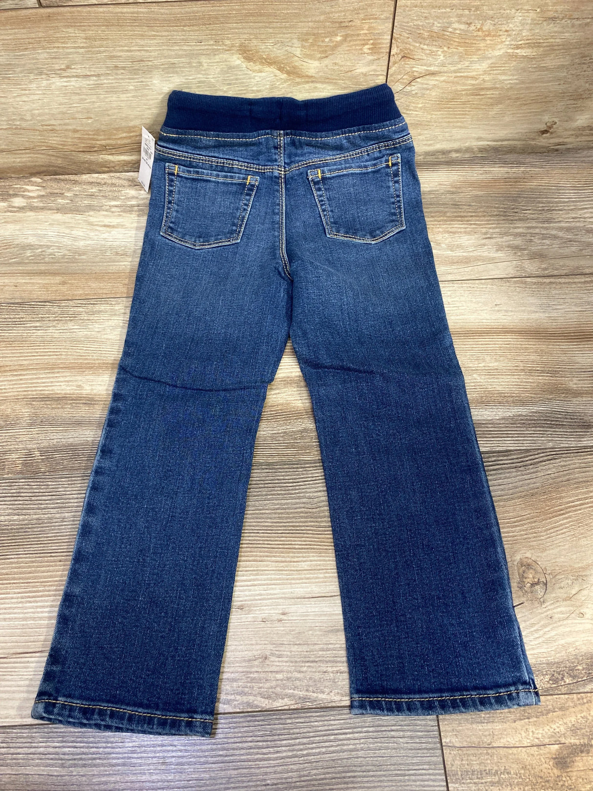 Back view of kids' blue denim jeans with elastic waistband and two pockets on wood floor