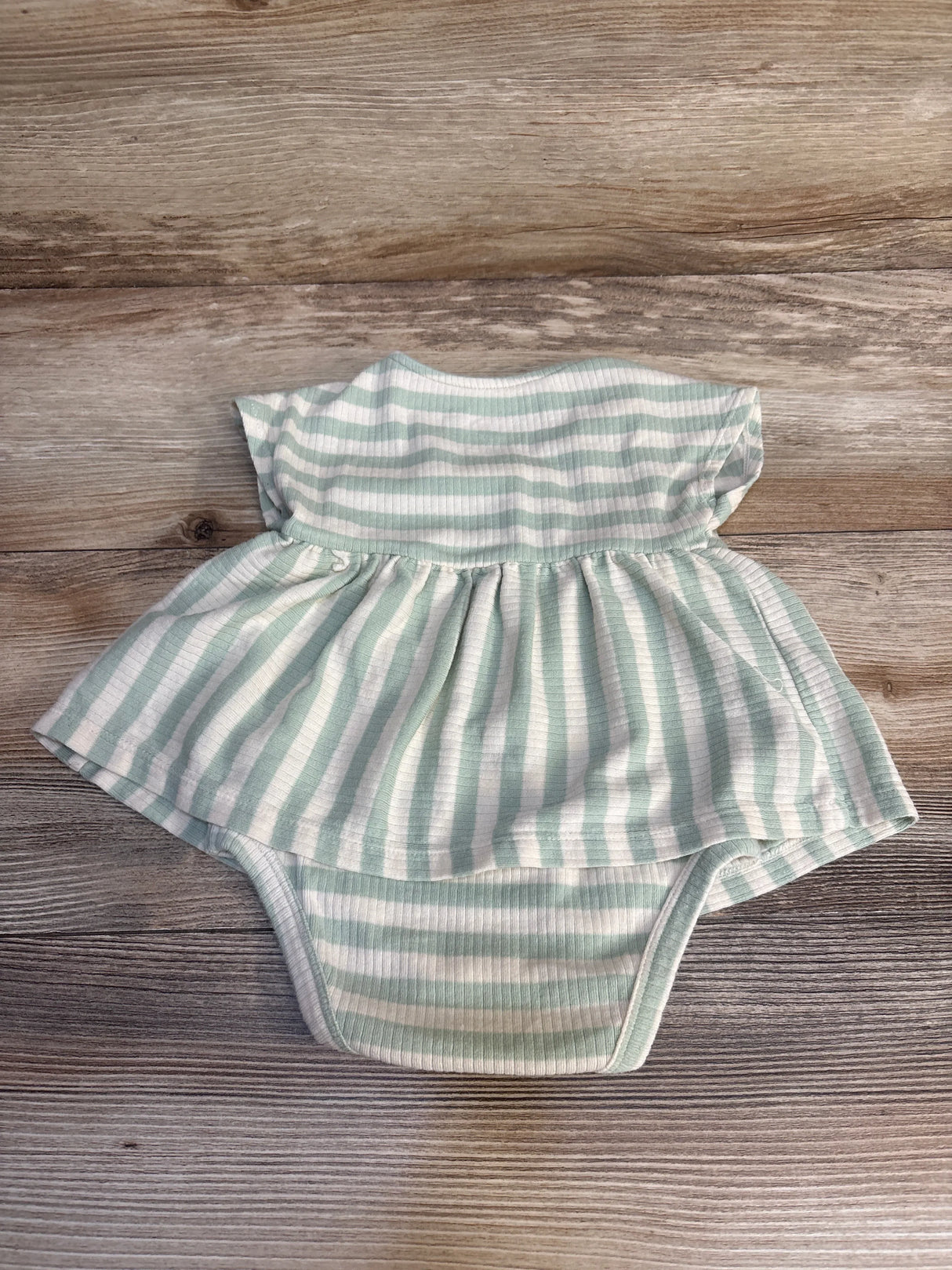 Mint green and white striped baby romper with ruffled skirt, laid on wood floor