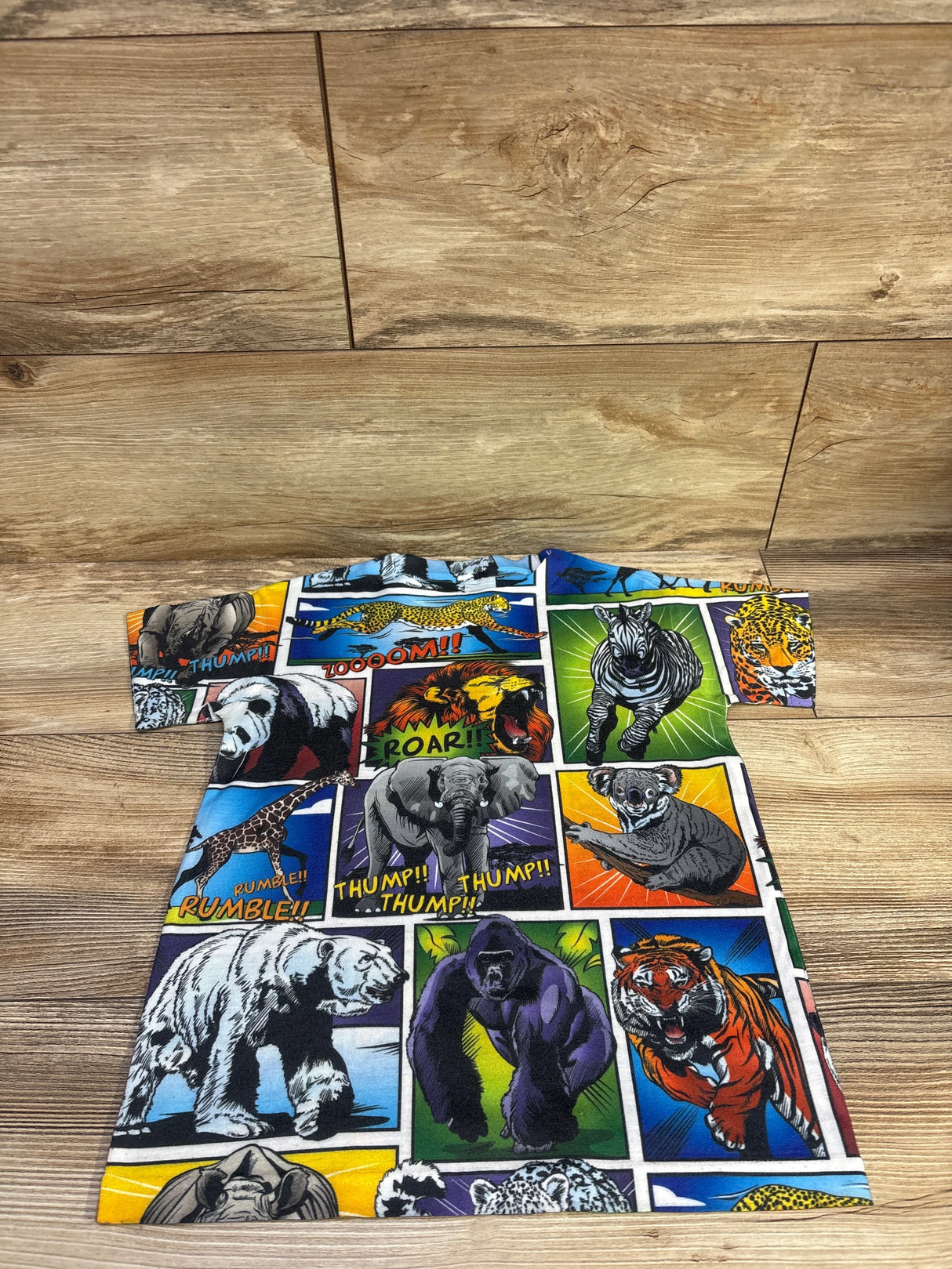 Front view of comic style animal print shirt in blue, showcasing short sleeves and colorful animal panels on a wooden floor