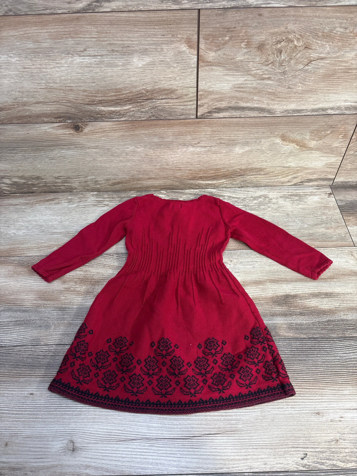 Red long-sleeve knit toddler dress with black floral embroidery on hem, laid on wooden floor