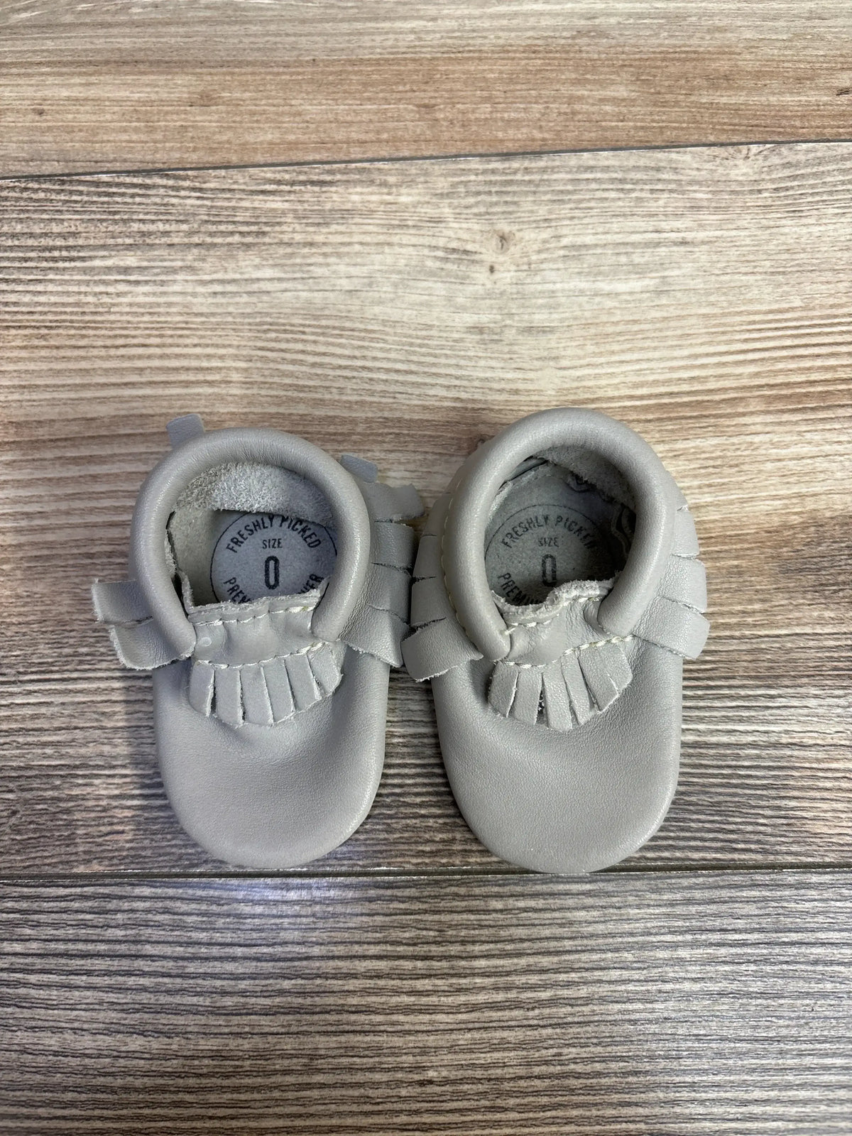 Pair of light gray leather baby moccasins size 0 on wooden surface from children's resale store