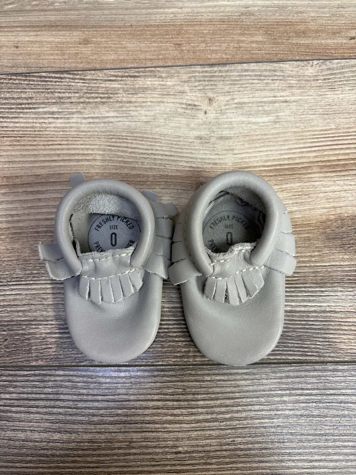 Pair of light gray leather baby moccasins size 0 on wooden surface from children's resale store