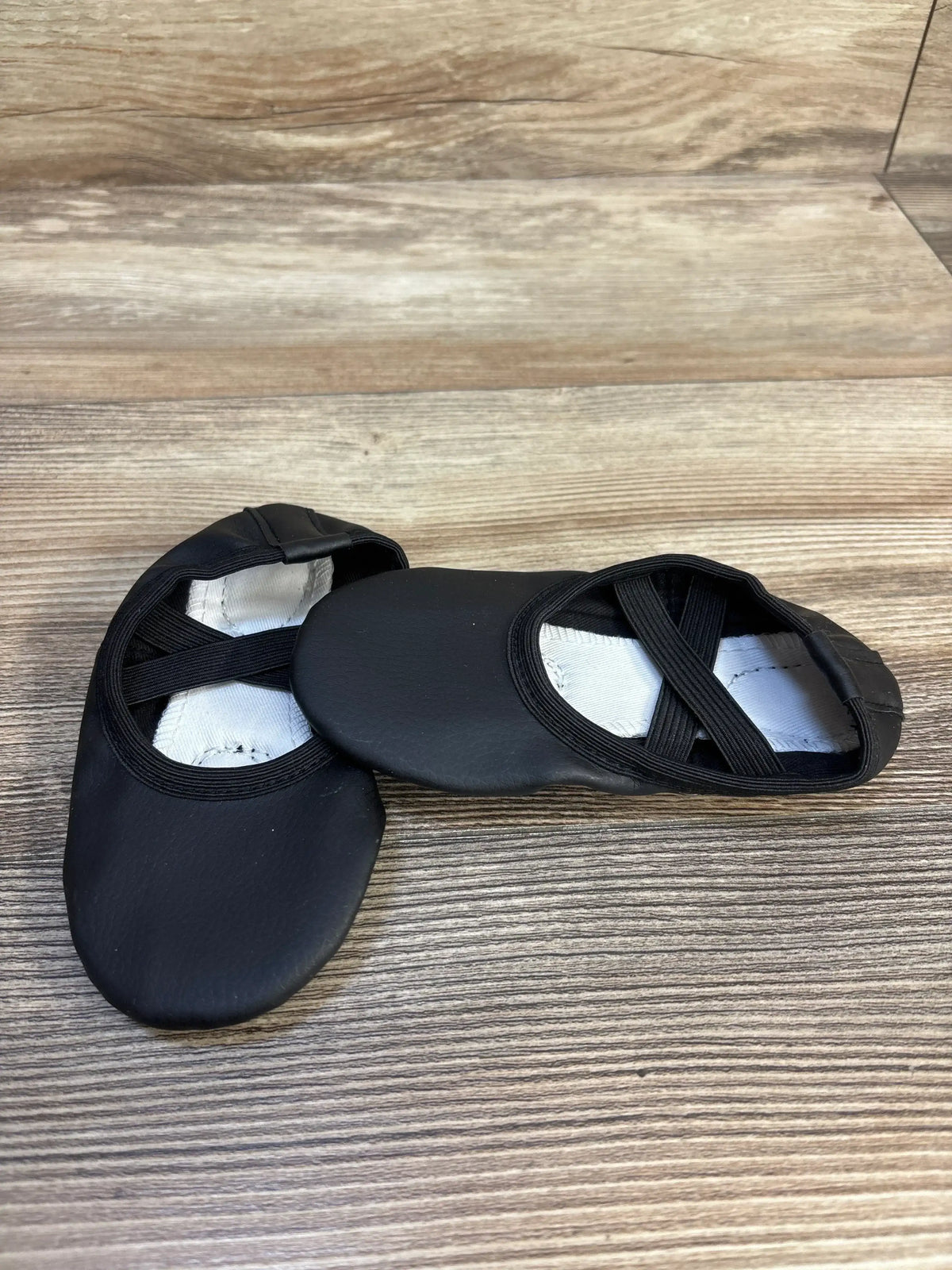 Black ballet shoes for kids with elastic straps on wooden floor