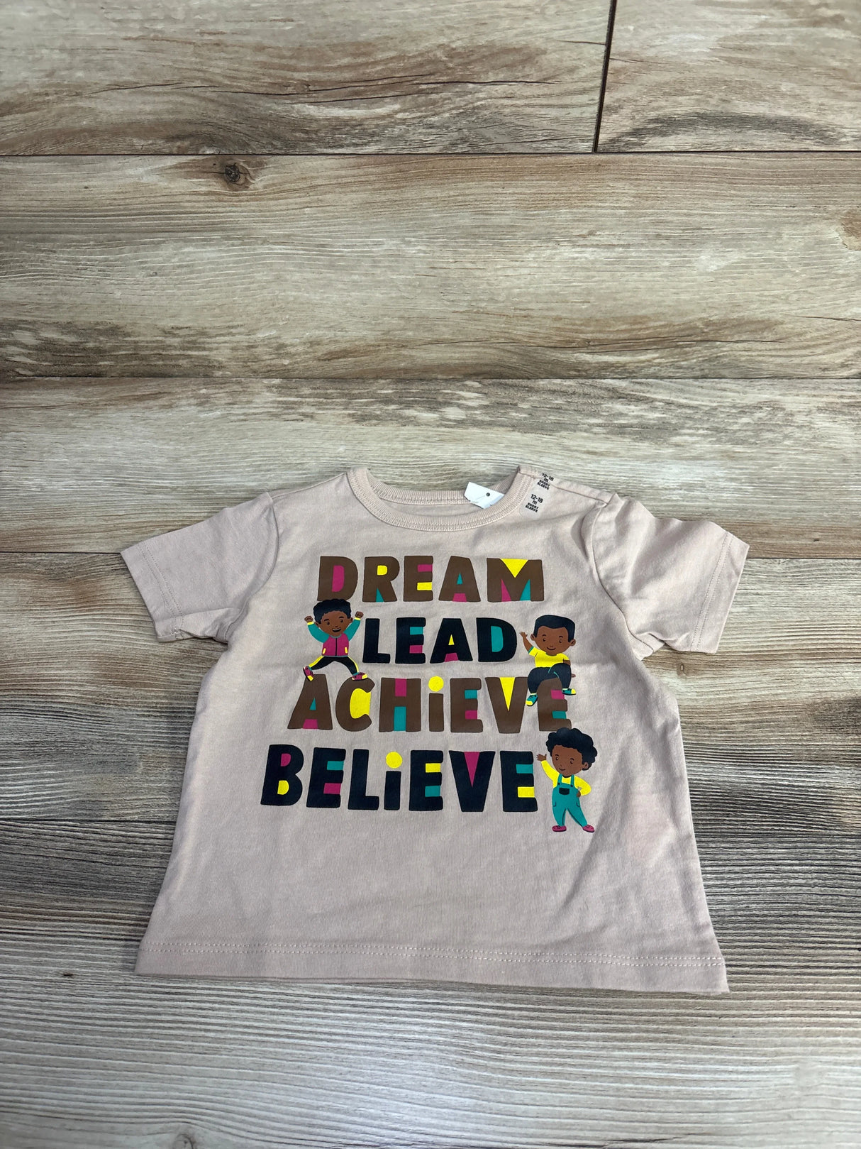 Beige toddler t-shirt with colorful letters saying Dream Lead Achieve Believe and three cartoon kids, kids clothing