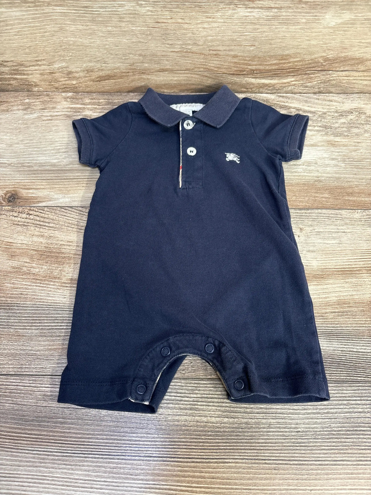 Flat lay of navy Burberry polo romper 3M showing polo collar, embroidered logo and snap leg closures on wood