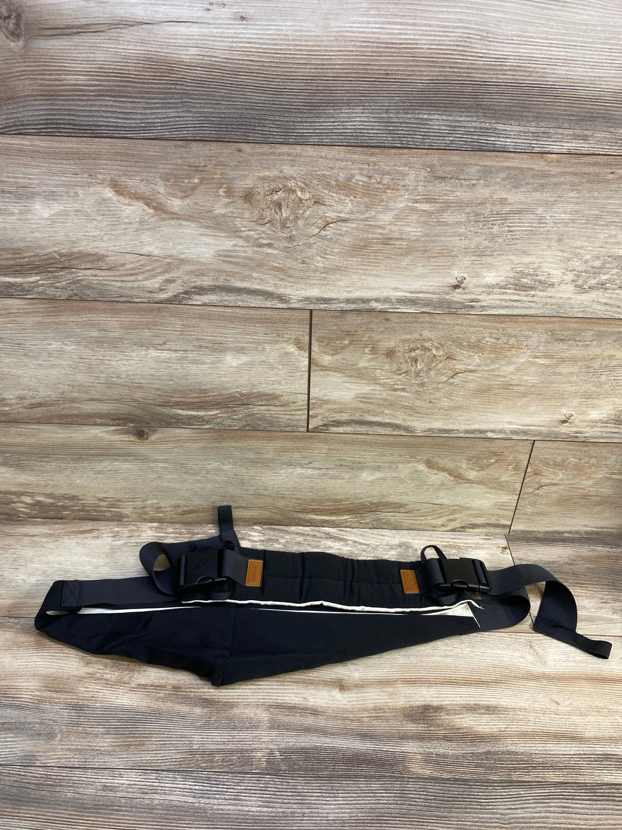 Flat lay of Bambora sling carrier showcasing adjustable straps, large buckles, and white trim on black fabric on wood background