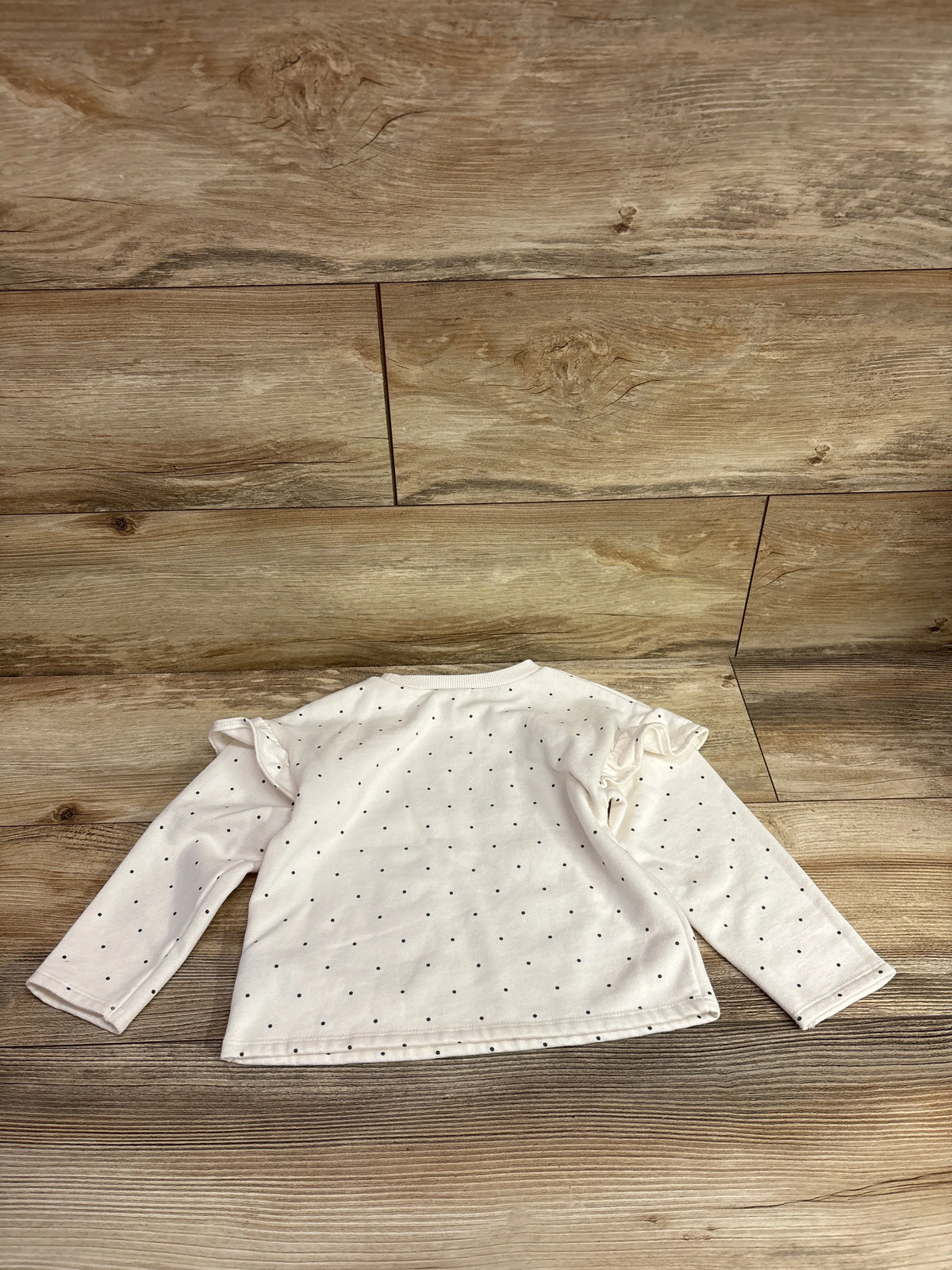 Flat lay of Carter’s white polka dot sweatshirt in size 3T showcasing long sleeves and ruffled shoulders on wood flooring