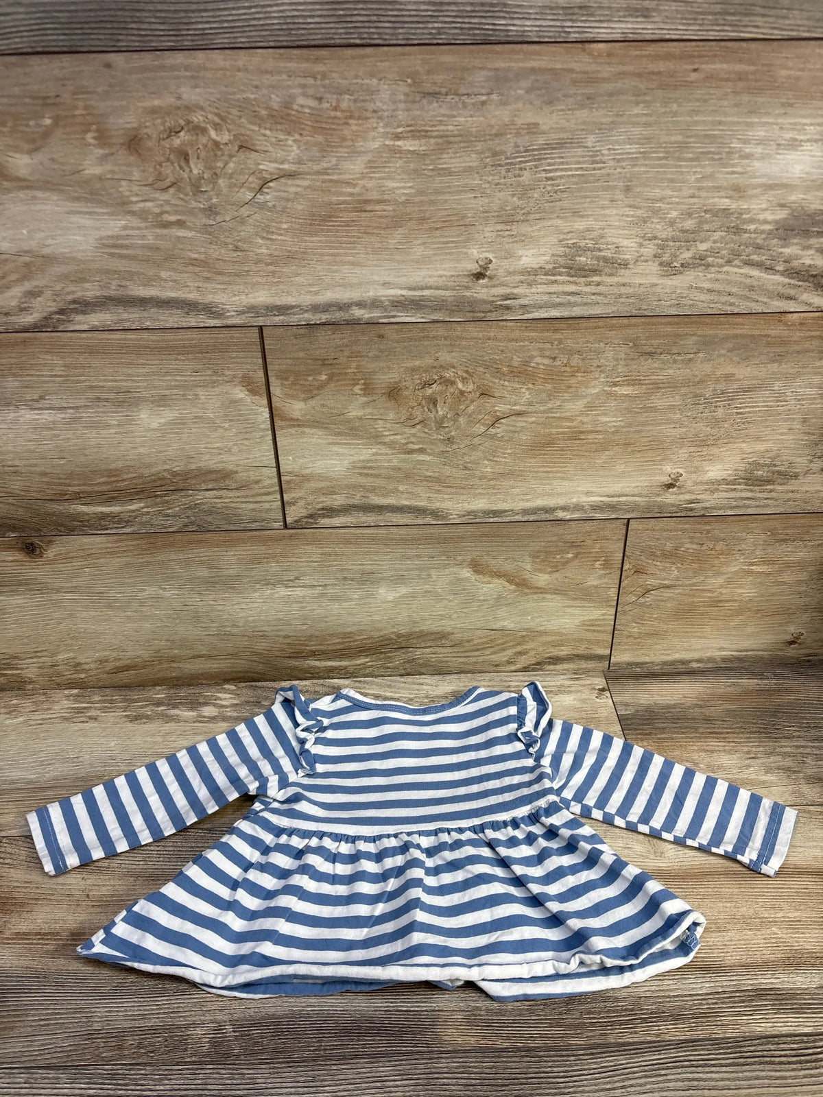 Front view of Durtebeua blue striped long sleeve peplum henley top with ruffled shoulders and flared hem on wood background
