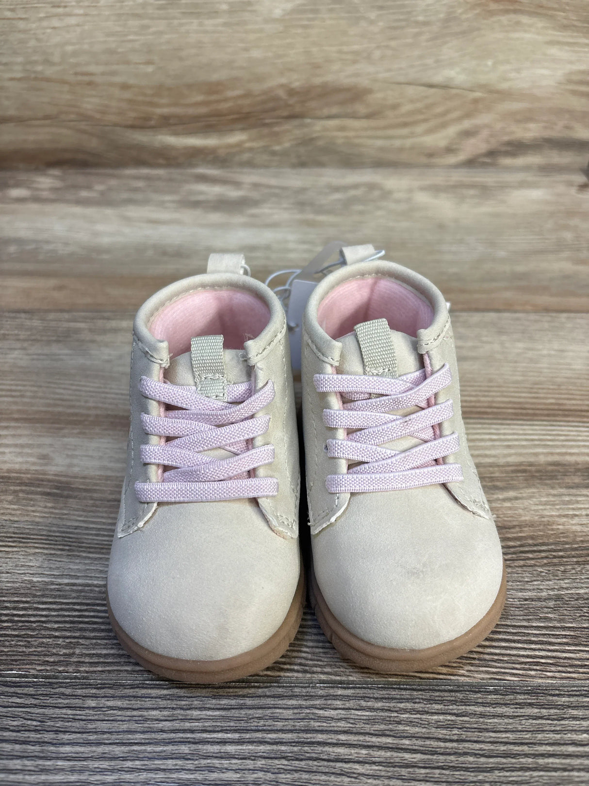 Pair of light beige toddler shoes with pink laces and soft brown soles on wood floor