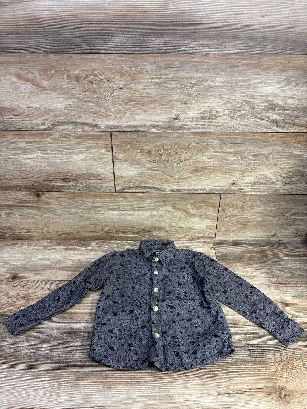Flat lay of grey toddlers' button-up shirt (4T) showing all-over space print, front pocket, and white buttons on wood background