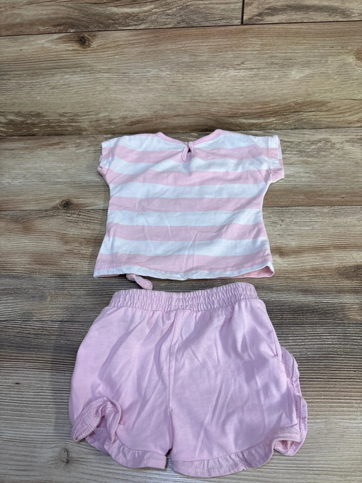 Back flat lay of pink baby 2-piece set: striped tee with keyhole button and knotted hem, solid elastic-waist shorts on wood