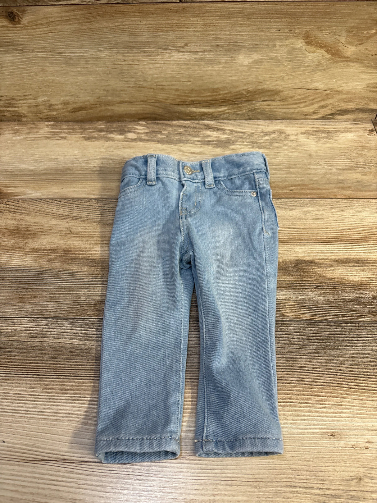Front view of Cat and Jack light-blue toddler jeggings (12 months) showing straight legs, belt loops and button on a wood surface