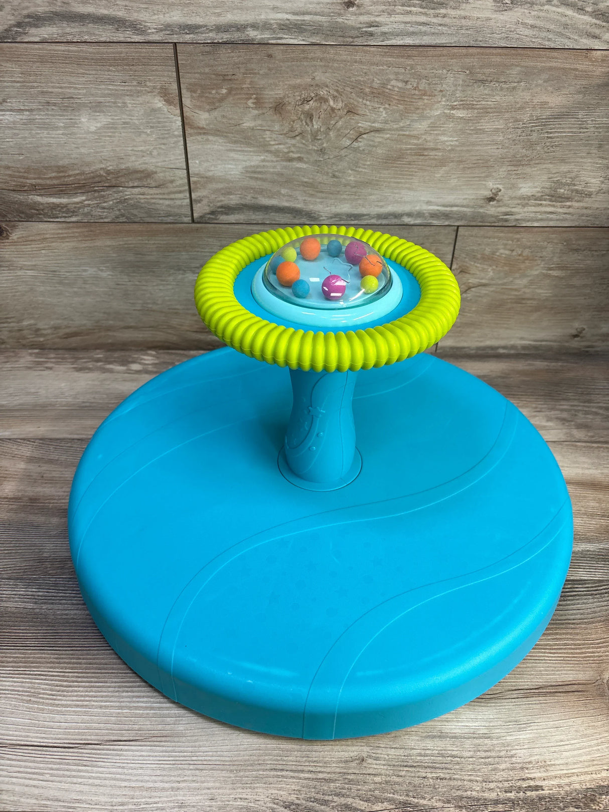Front view of B Toys Twirly Time spinning toy showing yellow ring and clear dome of colorful balls on turquoise base