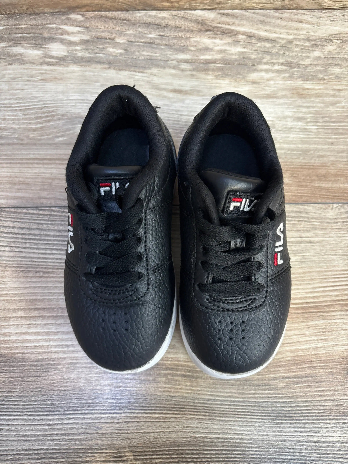 Pair of black Fila toddler sneakers with white soles on wooden floor