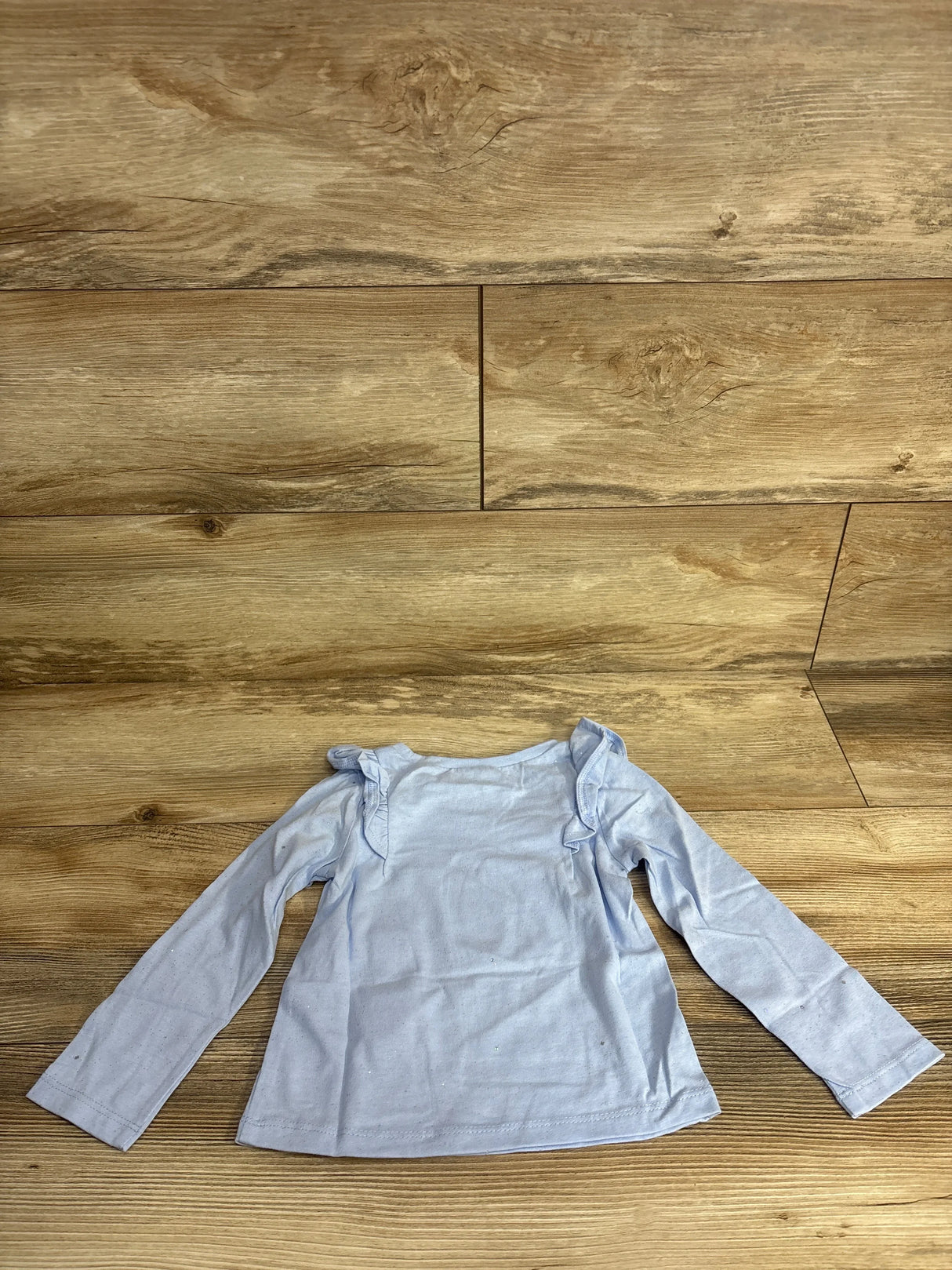 Light blue long sleeve toddler shirt with ruffle shoulder details on wooden background