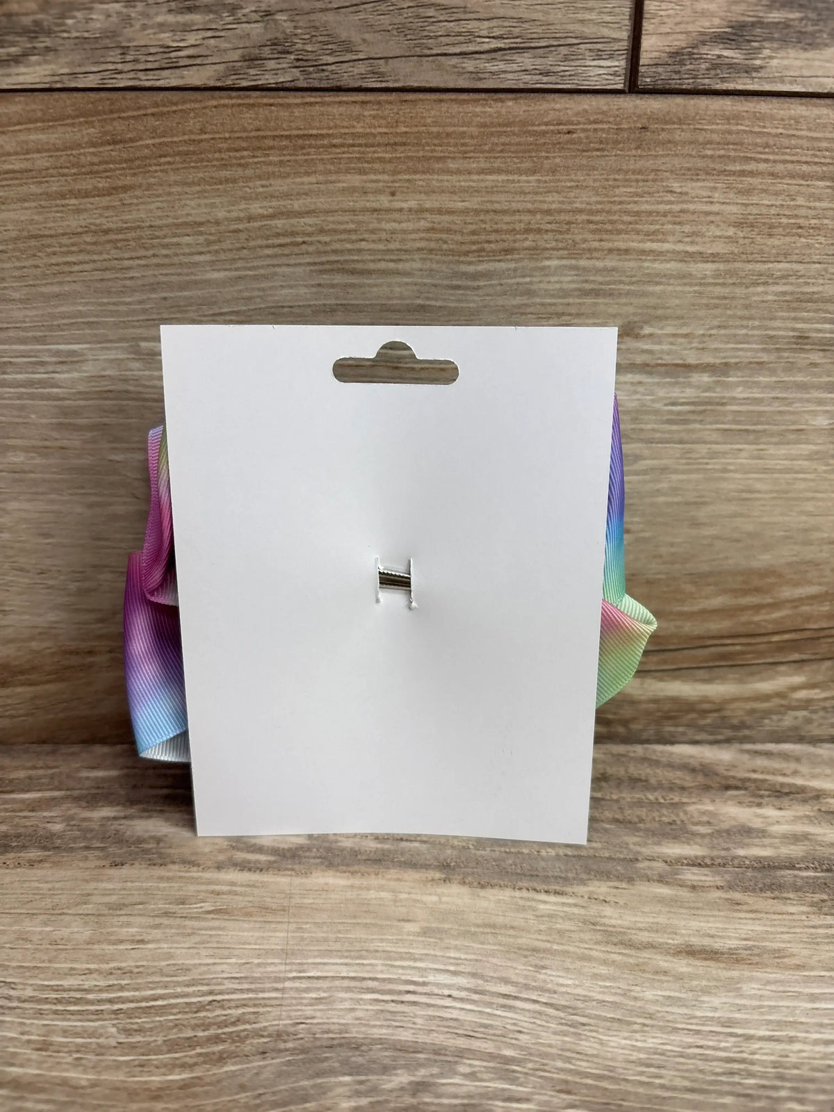Back view of NEW Large Hair Bow on blank white display card showcasing rainbow gradient grosgrain ribbon edges and metal clip on wood plank floor