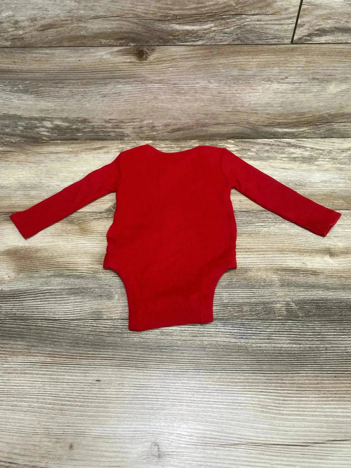 Flat lay of red rib-knit long-sleeve baby bodysuit (3-6 months) showcasing ribbed texture and snap crotch on wood background