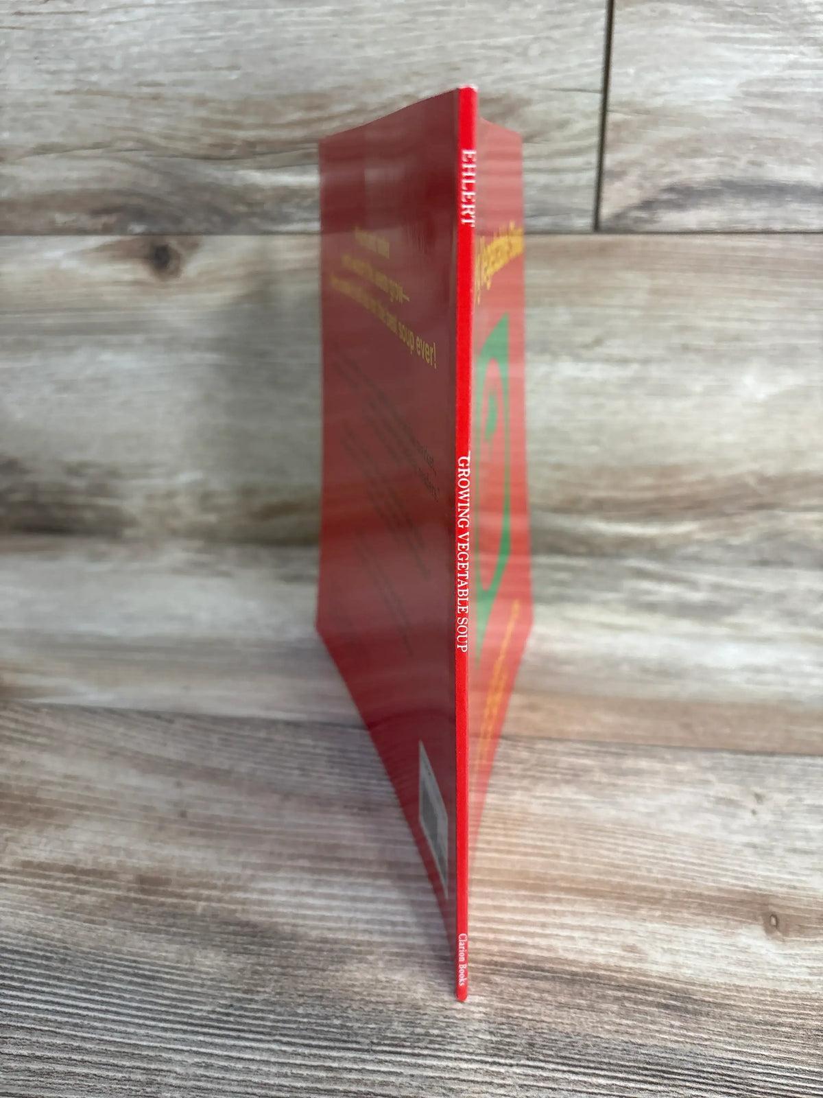 Slim red book titled Growing Vegetable Soup standing on wooden surface with faint text and barcode visible