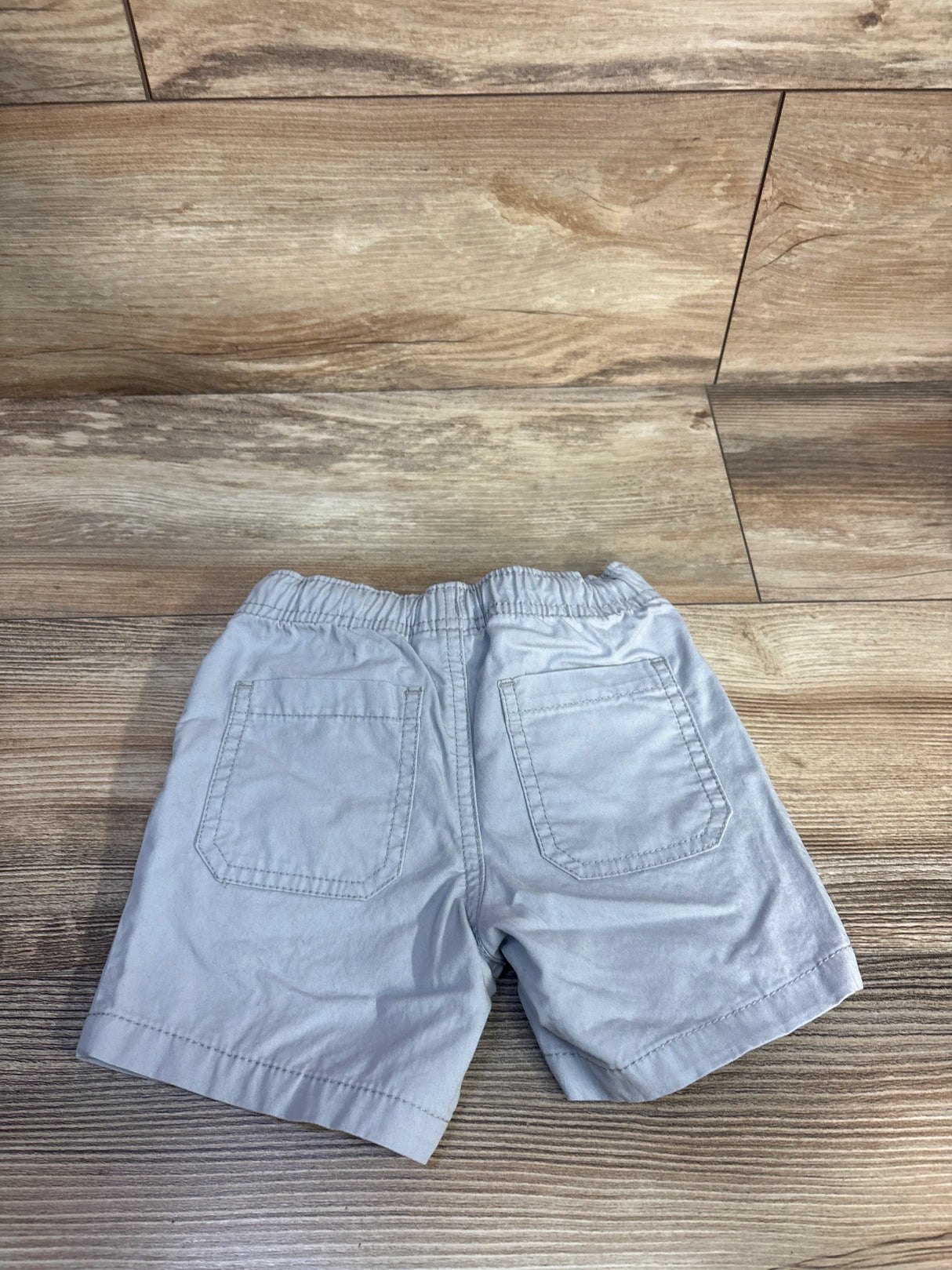 Back view of grey Cat & Jack drawstring shorts size 18 months showing elastic waistband and back patch pockets on wood