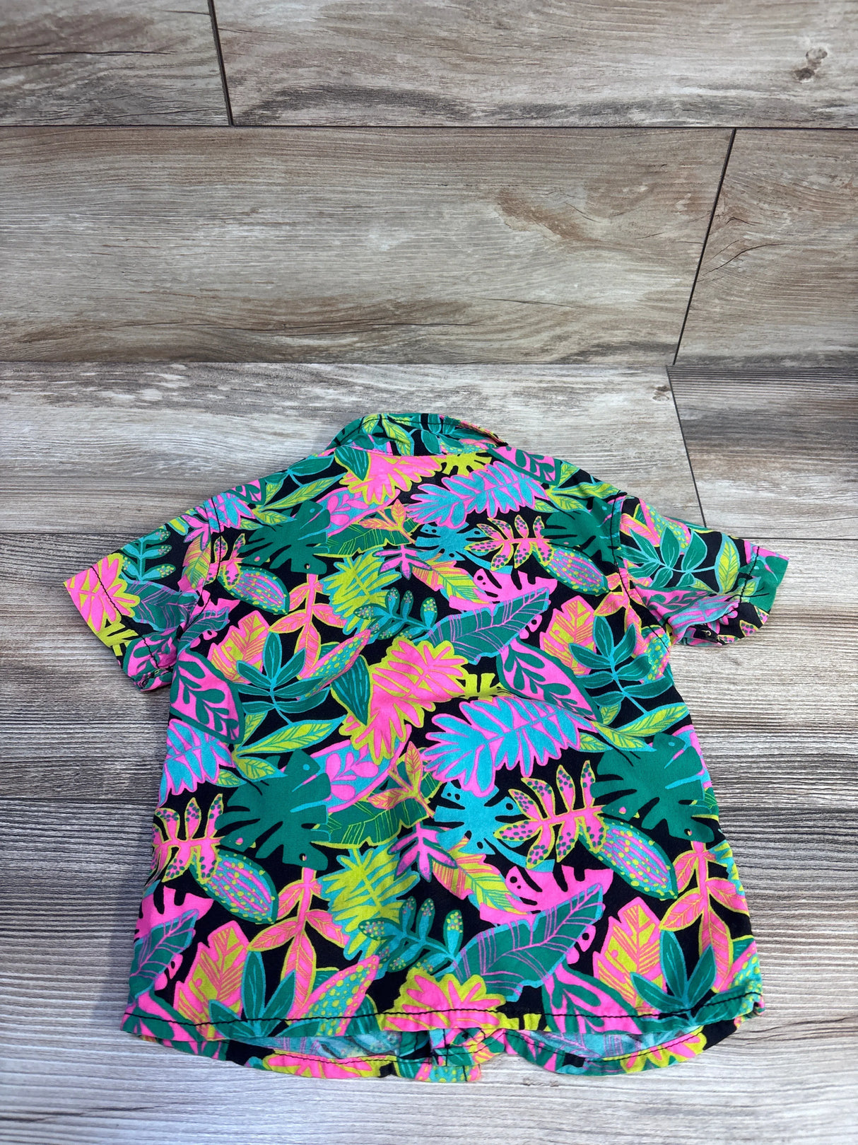 Back view of Cat & Jack toddler short-sleeve button-up shirt showcasing bright tropical leaf print on wood plank background