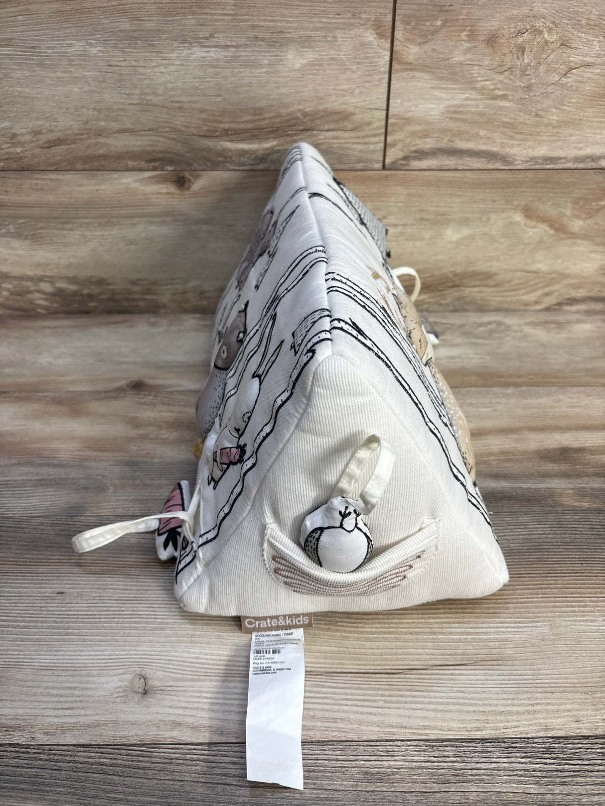 Side view of Crate & Kids Woodland Animals tummy time wedge showcasing triangular soft fabric with attached plush toys on wooden floor
