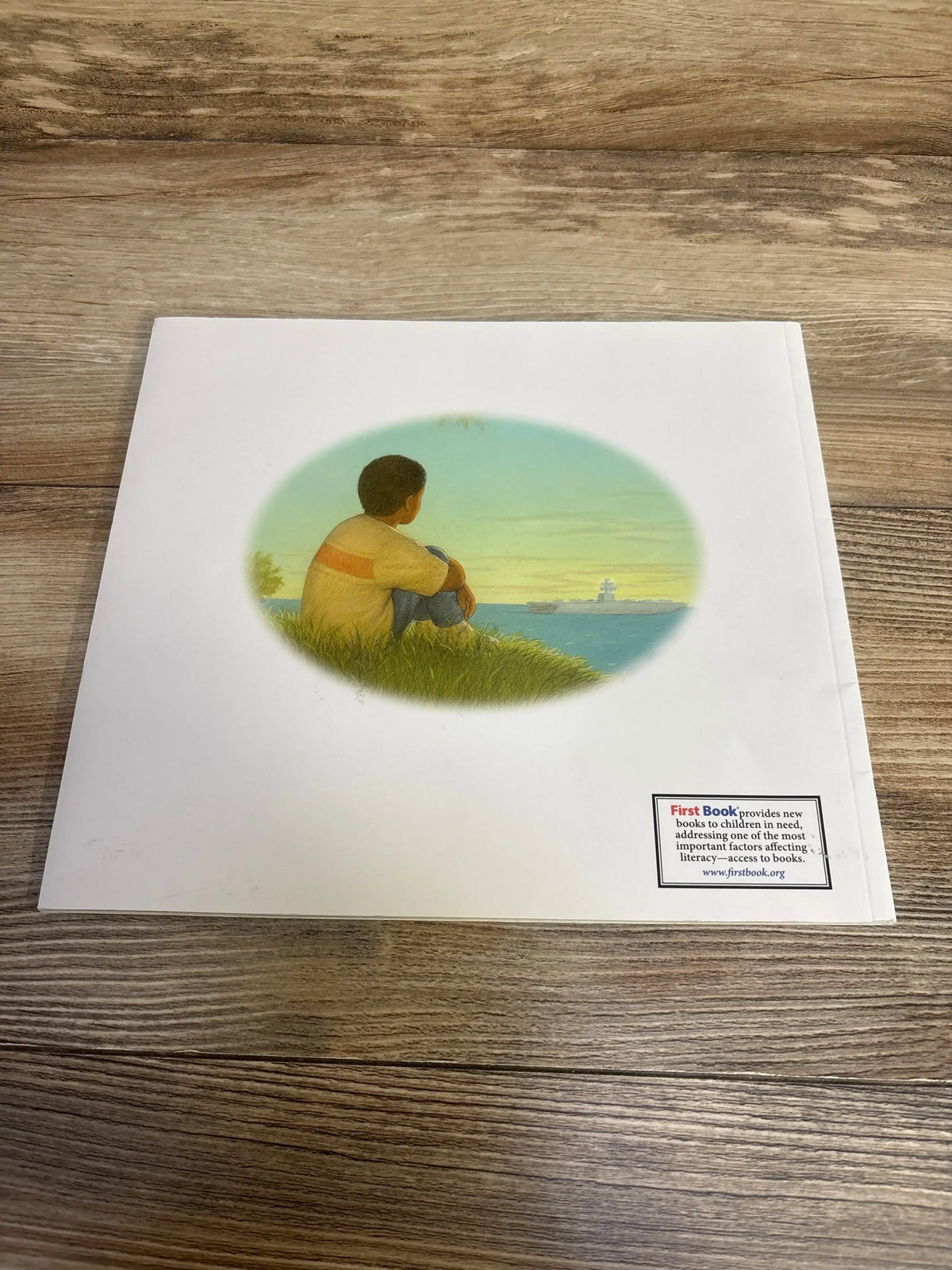 Flat lay of While You Are Away paperback showcasing front cover illustration of a boy looking at a ship on a wood tabletop