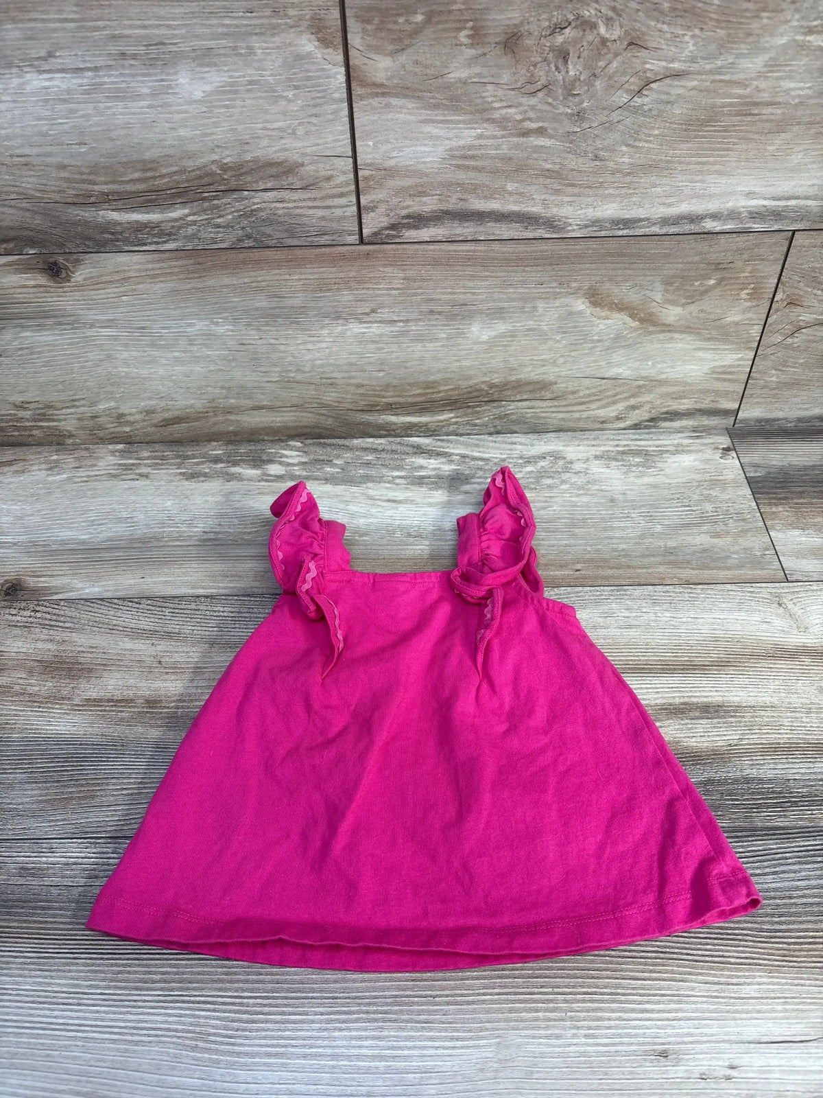 Flat lay of hot pink jersey top size 2T showcasing ruffled shoulder straps on wood plank background