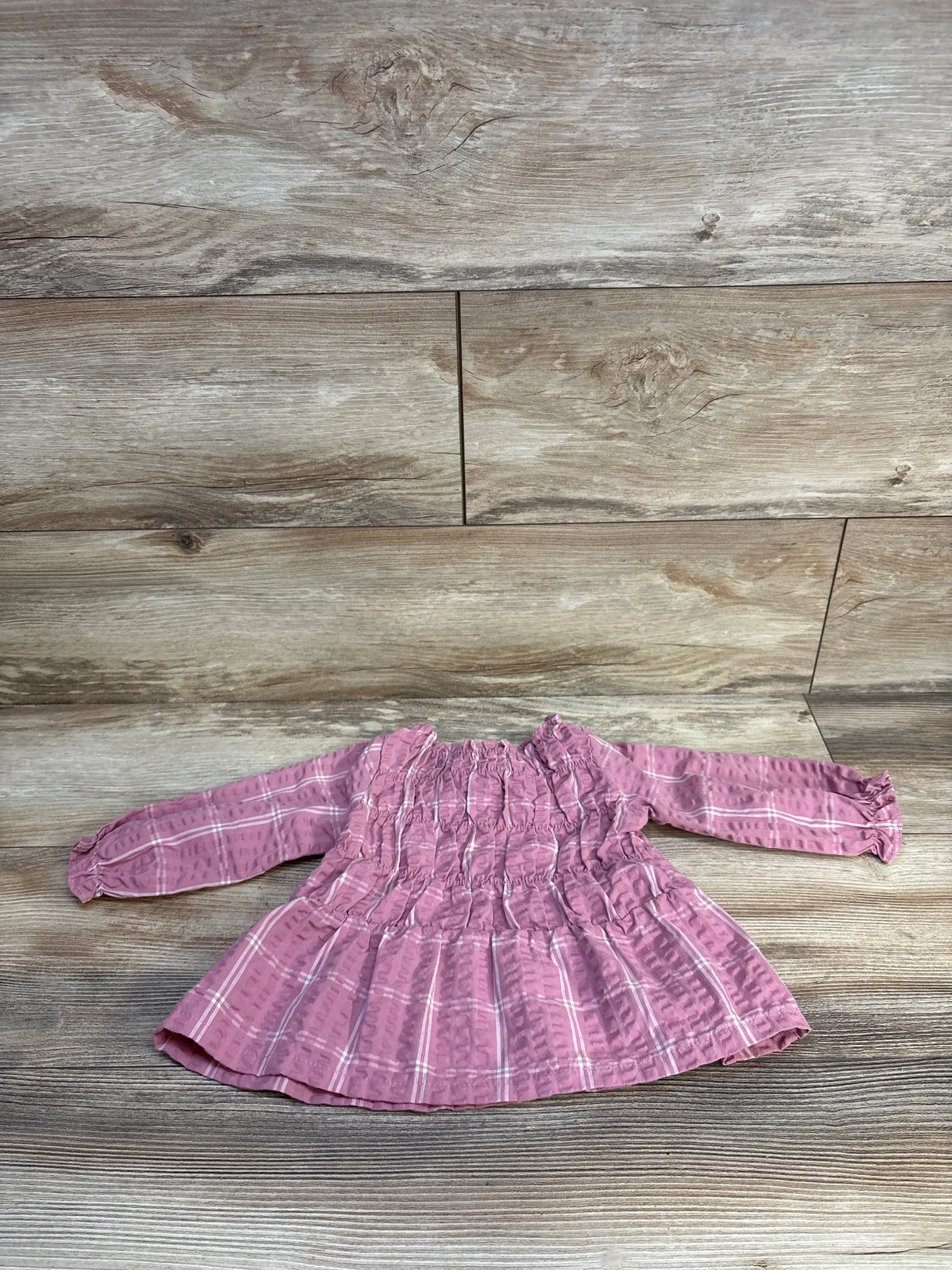 Pink plaid baby dress with smocked bodice and long sleeves on wood floor
