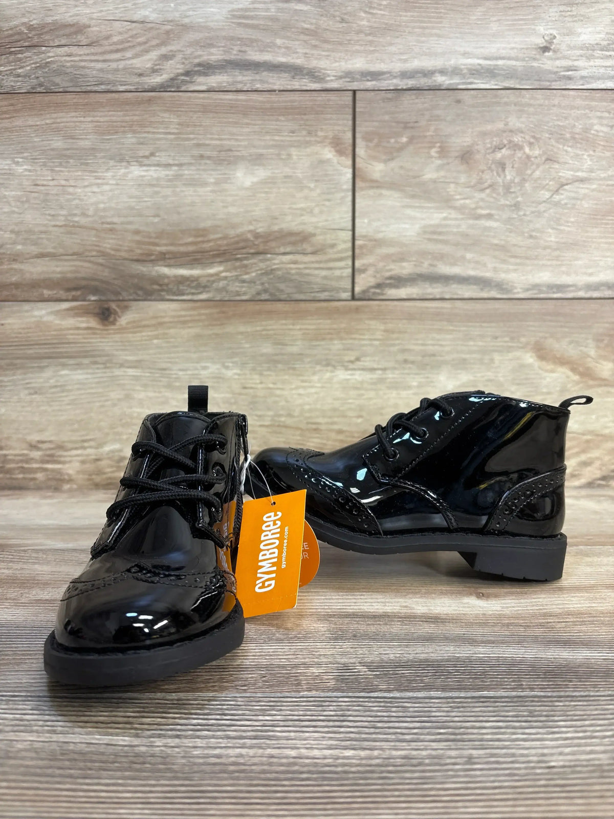 Black patent leather toddler dress shoes with laces and Gymboree tag on wood floor