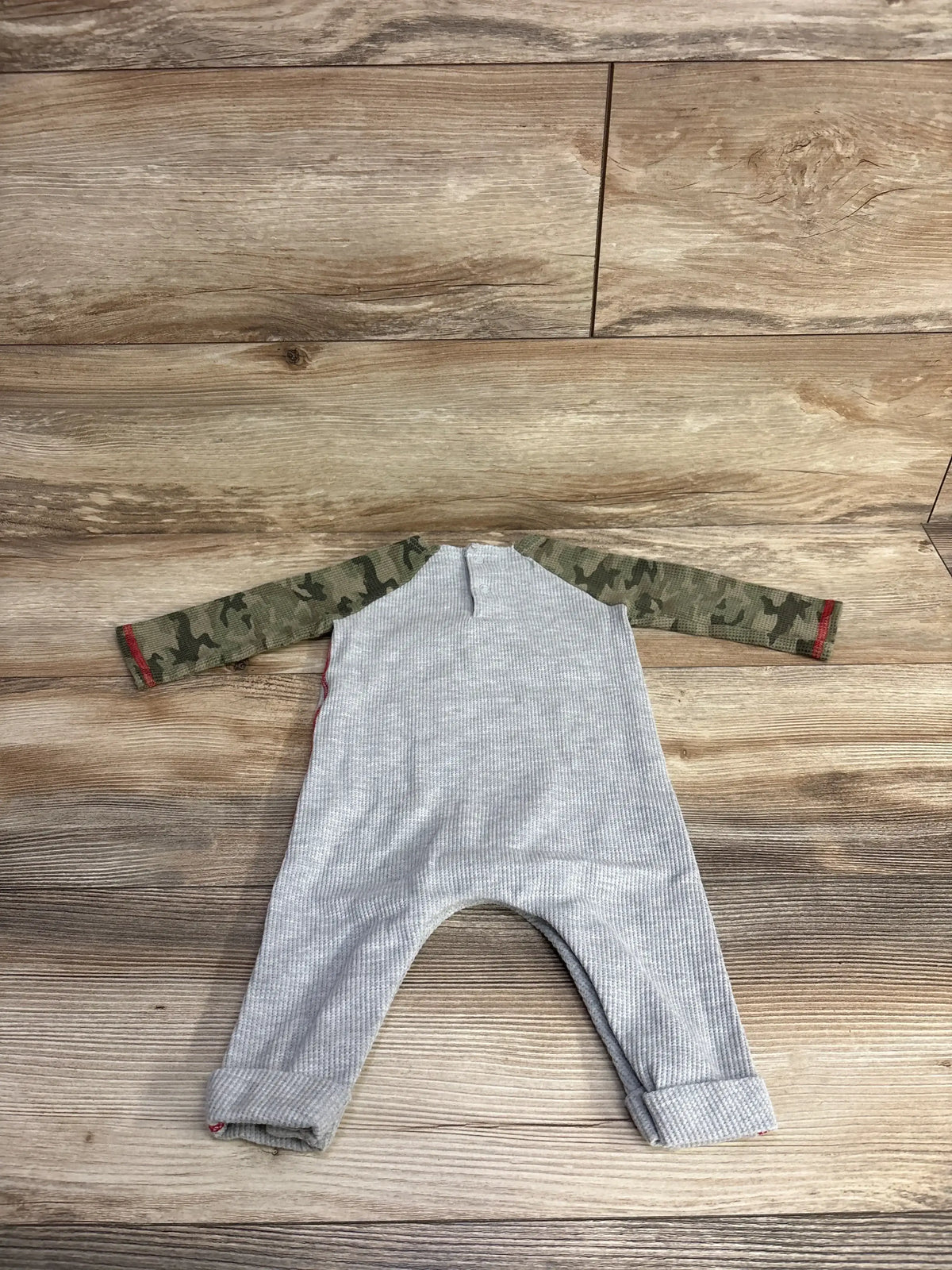 Gray baby onesie with camouflage sleeves on wooden floor