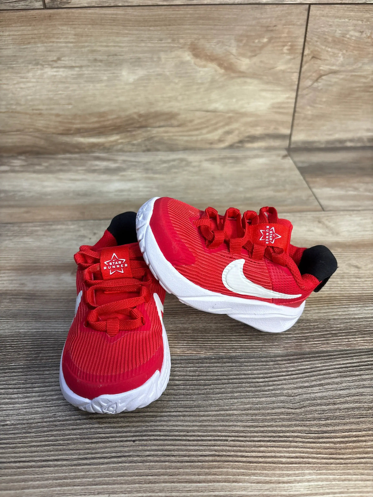 Front and side view of University Red Nike Star Runner 4 TD sneakers with red mesh uppers and white soles on wood flooring