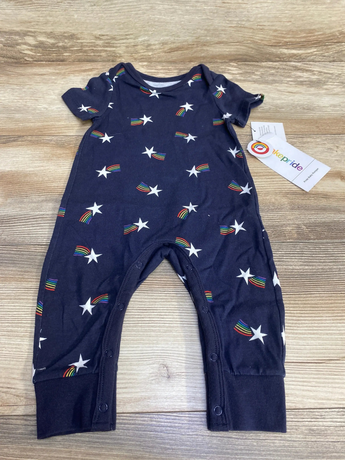 Front view of Takepride romper showcasing navy fabric with white star and rainbow print and hangtag on wood plank floor