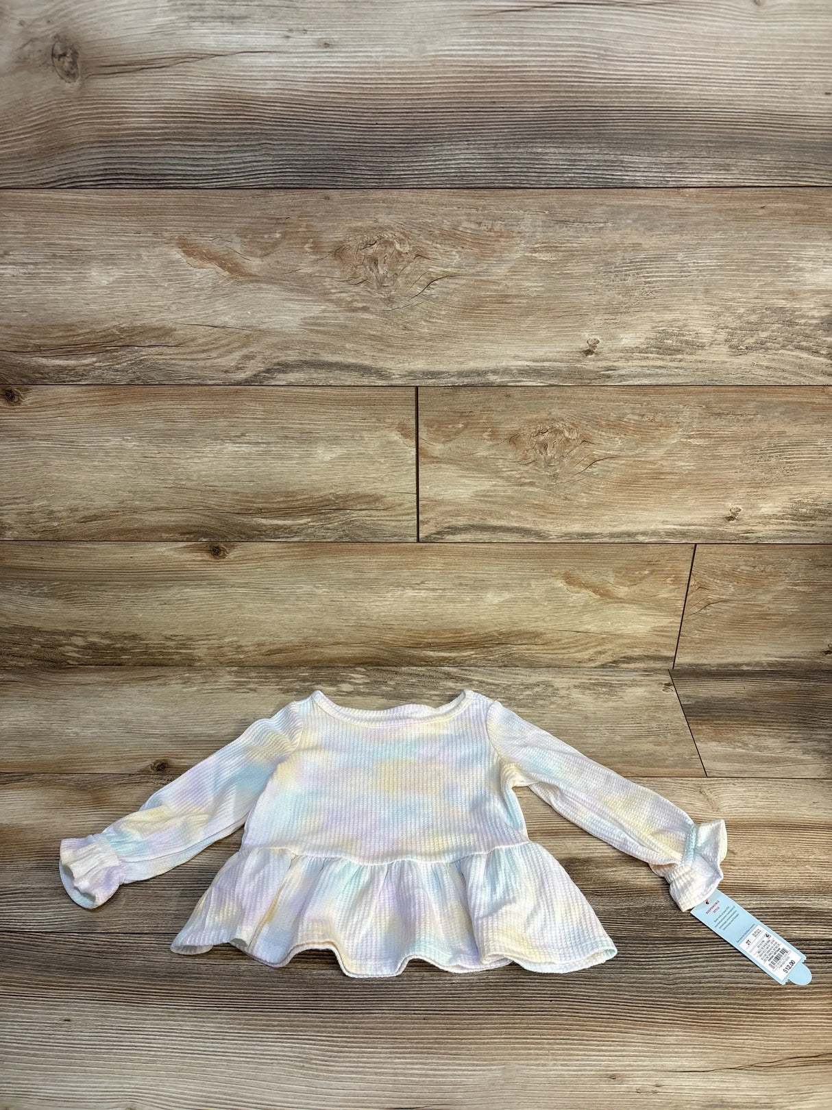 Long sleeve pastel tie-dye baby peplum top with tag on wood background