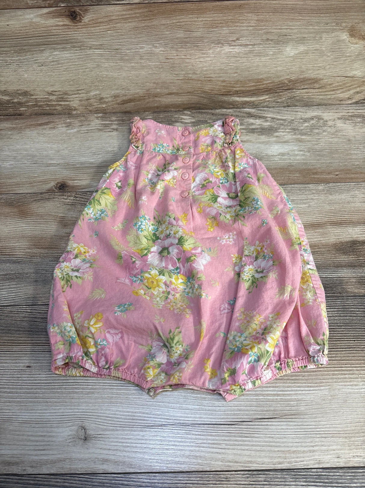 Pink floral baby romper with ruffled straps on wood background, gently used kids clothing